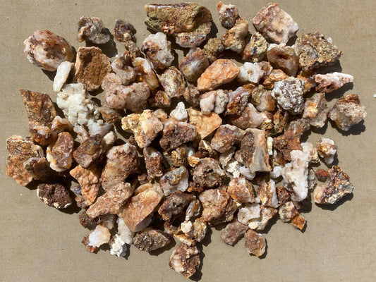 A pile of rough mineral and stone chips in earthy brown, beige, and white tones, photographed from above on a tan surface.