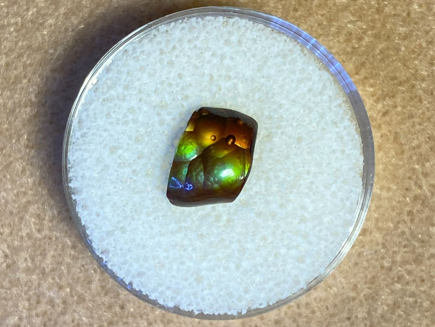 Multicolored Deer Creek fire agate gemstone on a white foam surface with a brown background