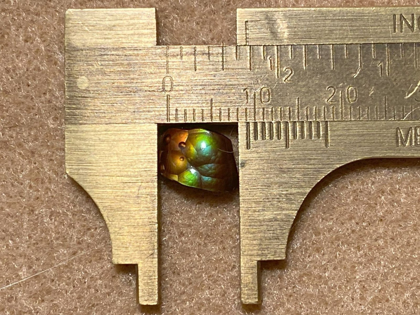 Small Deer Creek fire agate gemstone being measured with a vernier caliper on a brown background