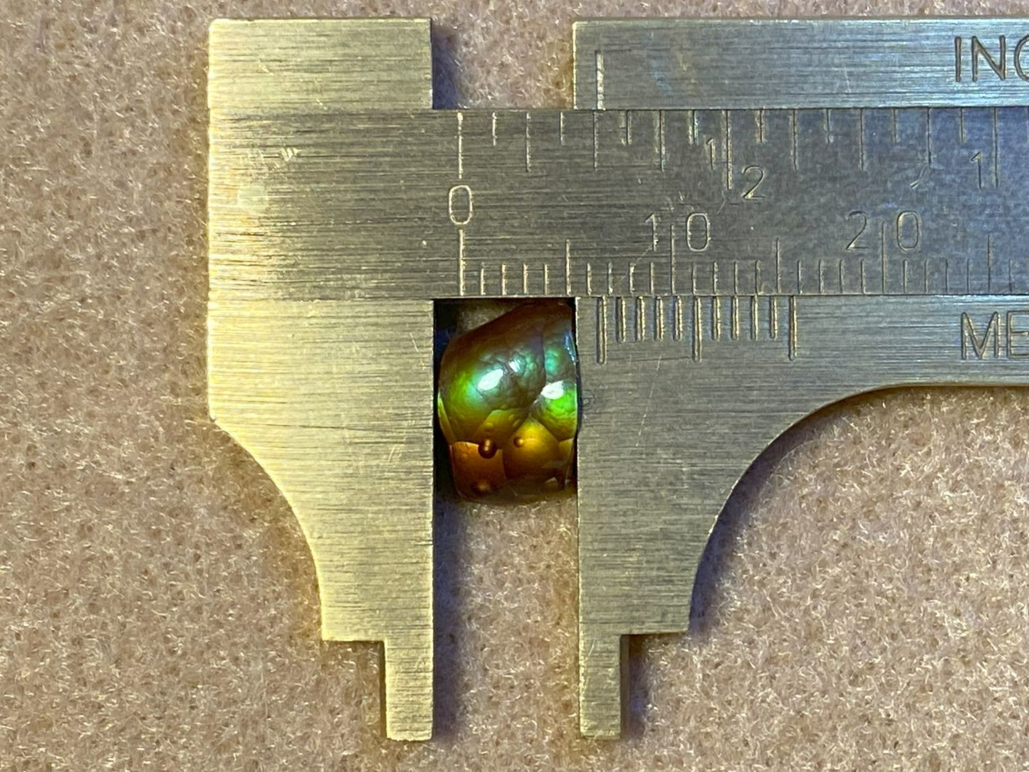 Close up of a brass ruler with a deer creek fire agate accent gemstone showing it measuring 5 millimeters in size