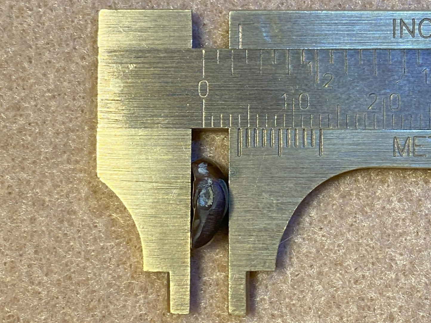 Metal vernier caliper measuring a small deer creek fire agate gemstone on a textured surface