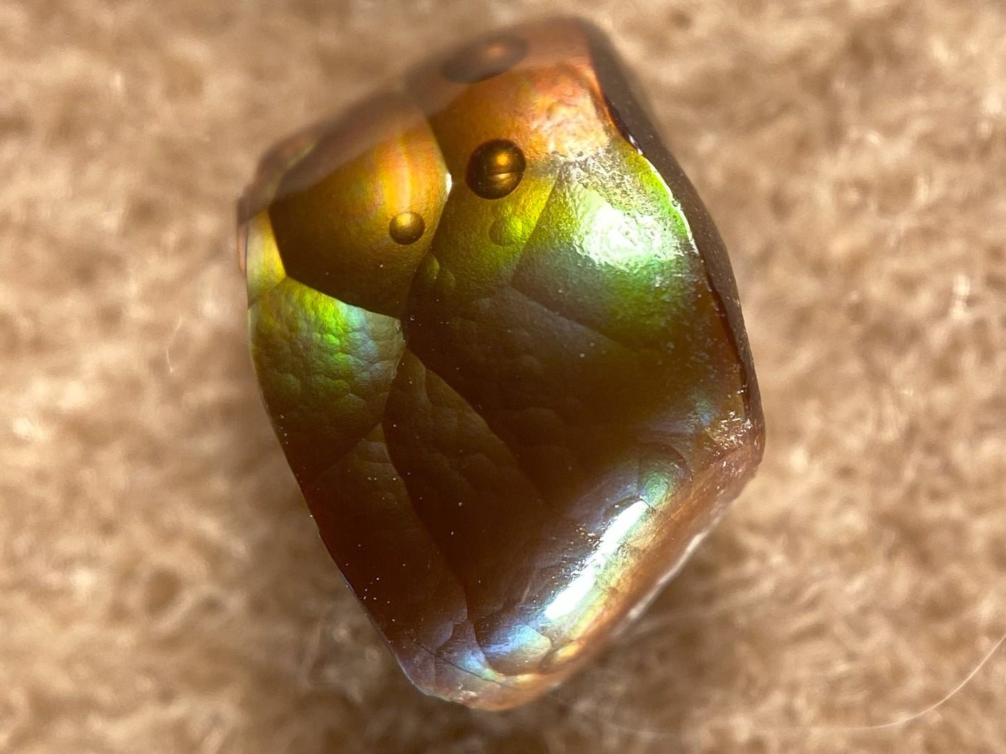 Multicolored deer creek fire agate loose gemstone with reflective surface on a beige background