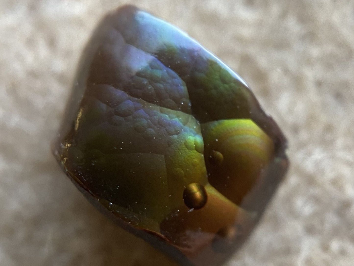 Multicolored Deer Creek fire agate gemstone on a beige surface