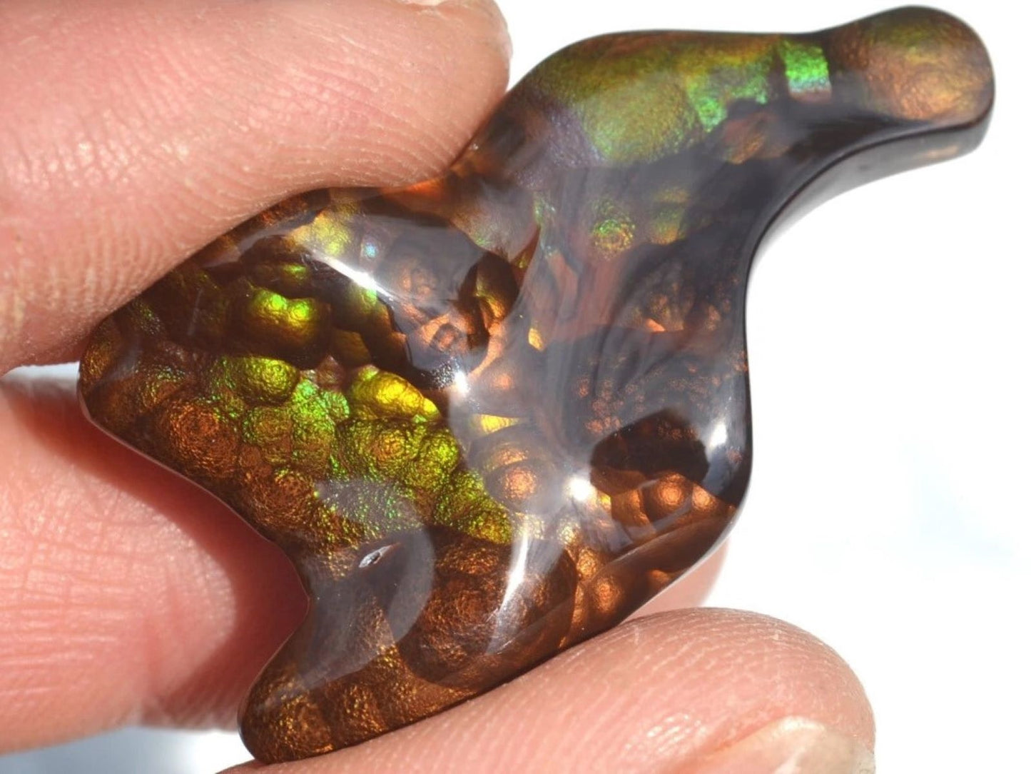Deer Creek fire agate gemstone held between fingers with a white background