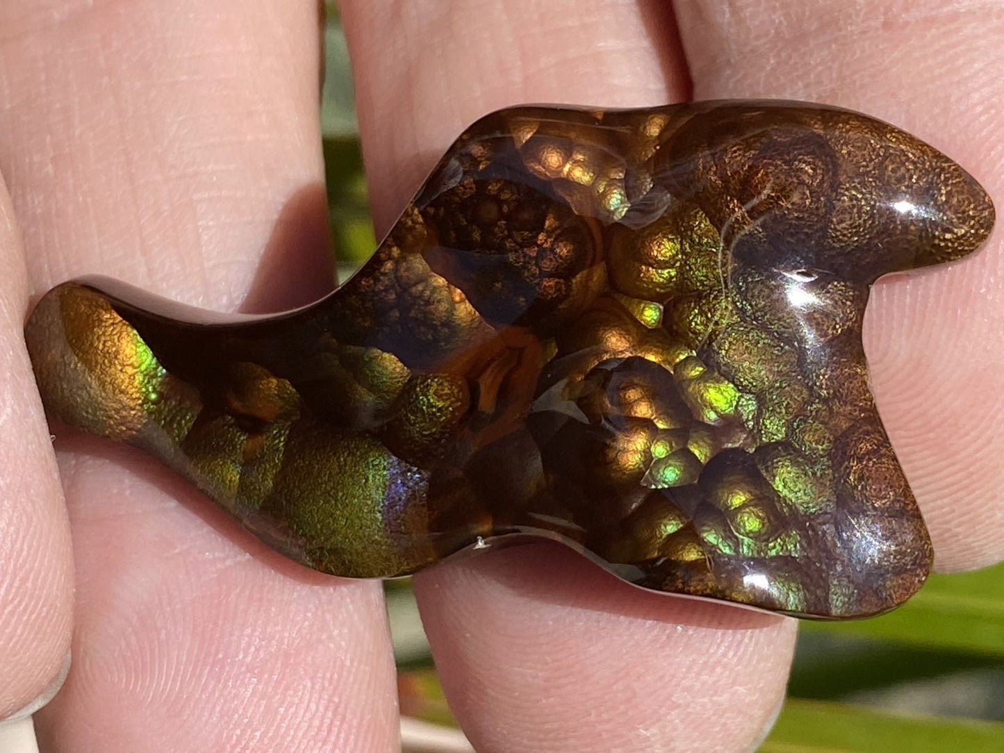 Polished Deer Creek fire agate gemstone with iridescent colors held between fingers