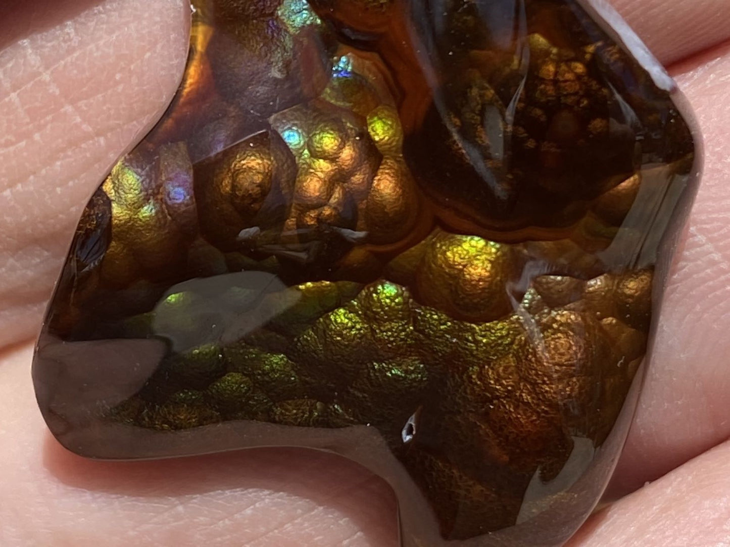 Close-up of a polished Deer Creek fire agate gemstone held between fingers