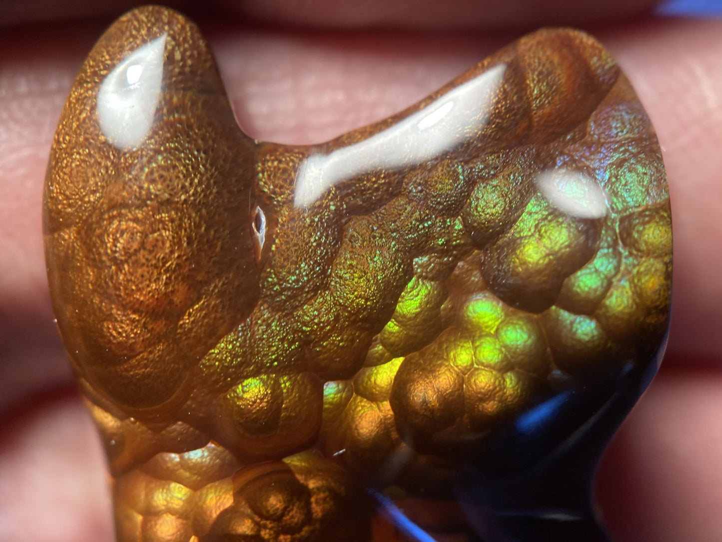 Close-up of a colorful Deer Creek gem stone with iridescent properties held between fingers.