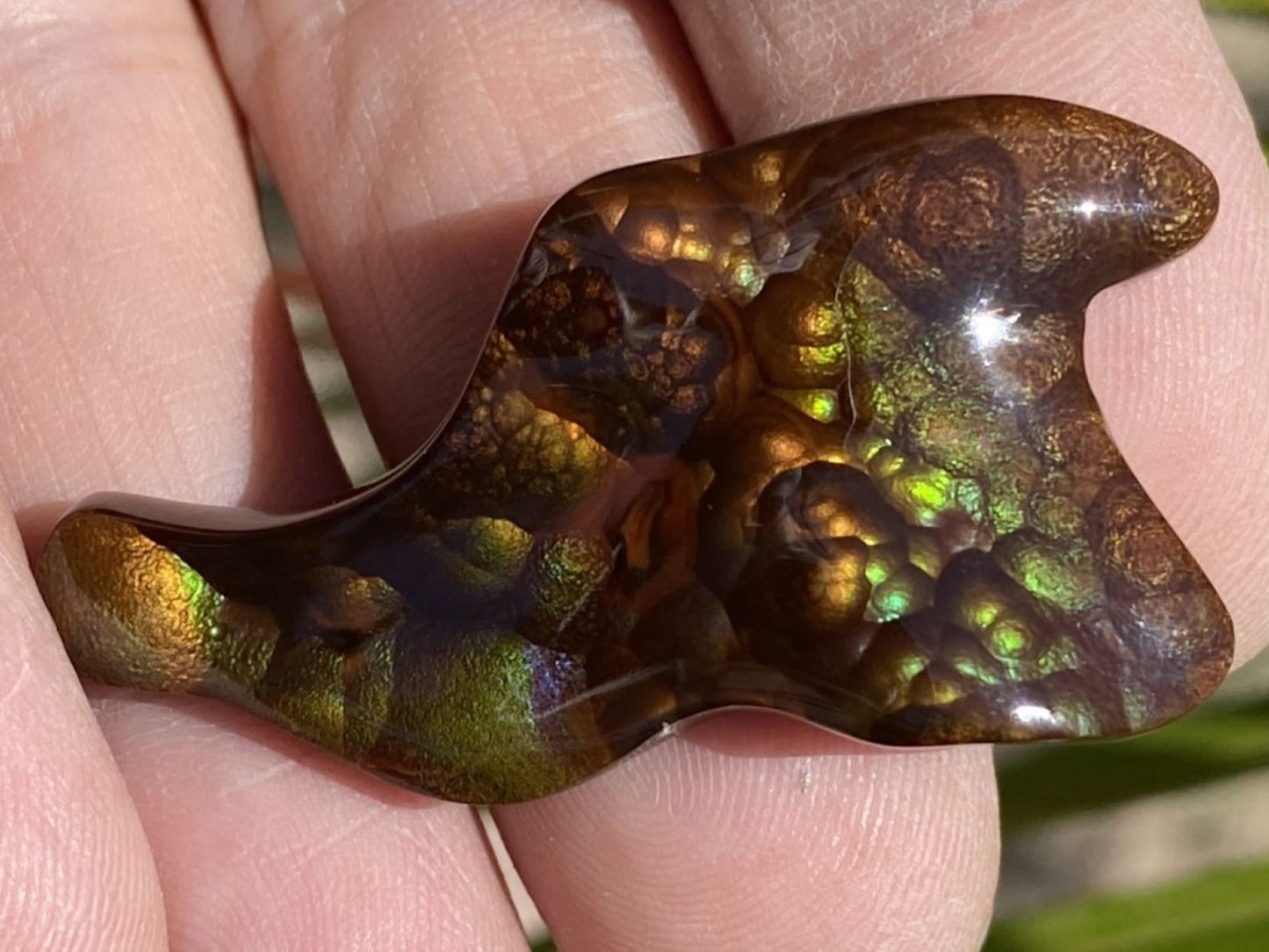 A colorful Deer Creek fire agate gemstone held between fingers with a natural background