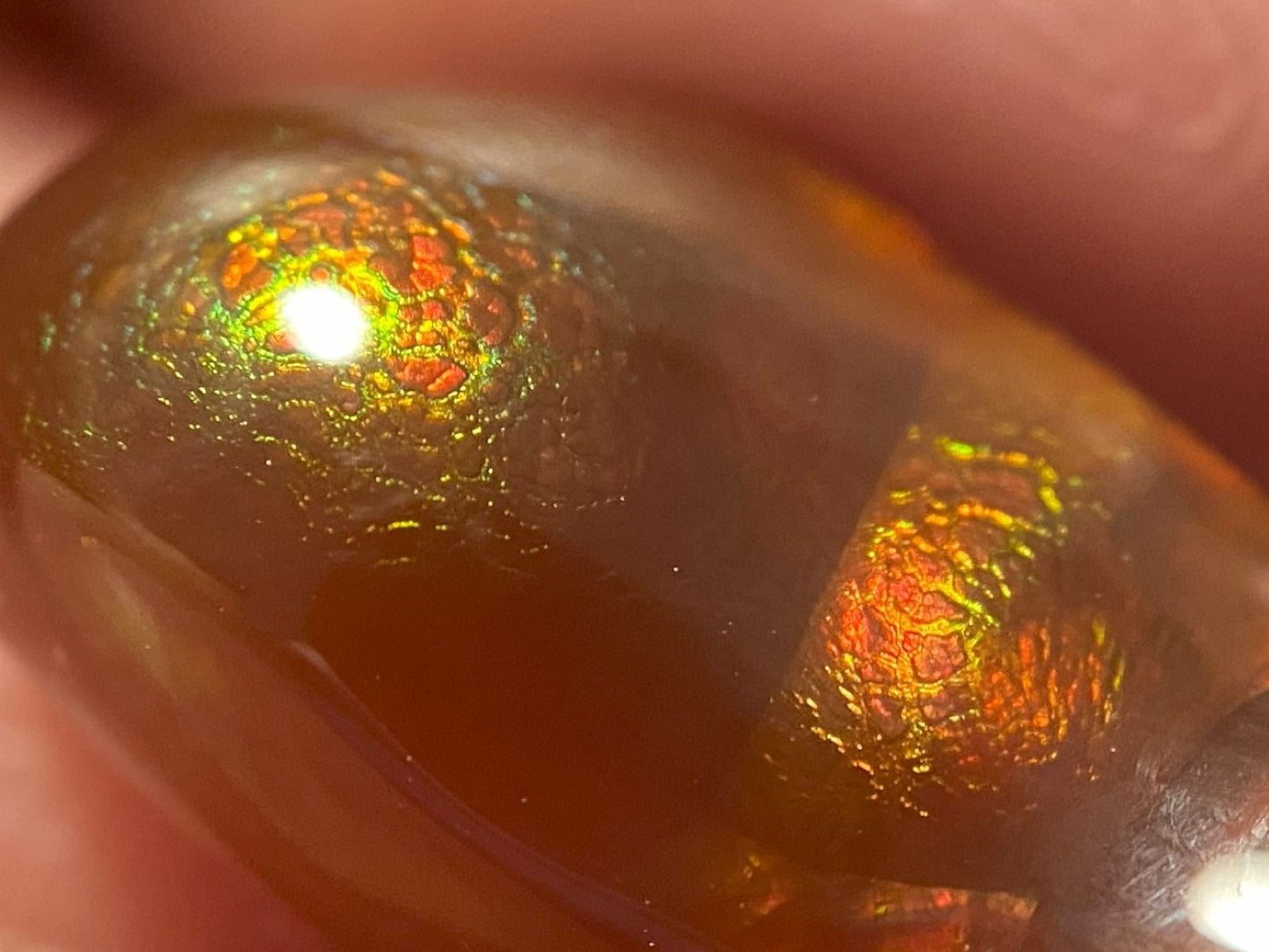 Close-up of a colorful, iridescent Deer Creek fire agate stone held between fingers