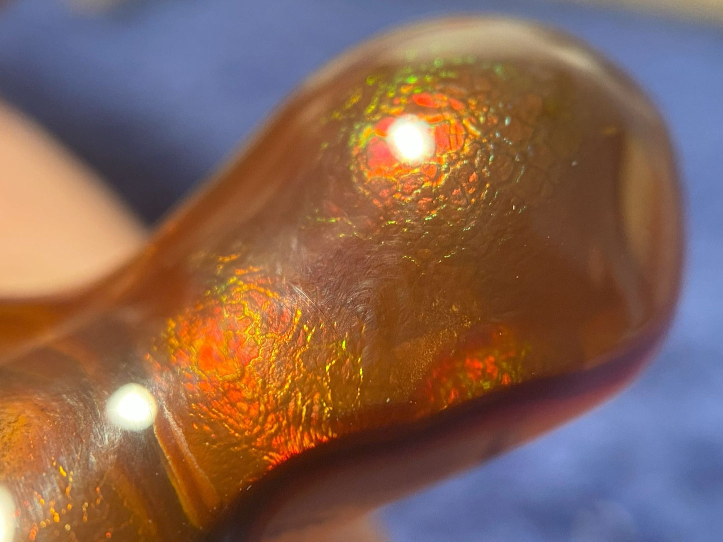 Close-up of a piece of fire agate gemstone with an iridescent red and green crackle patterns on a blurred background.