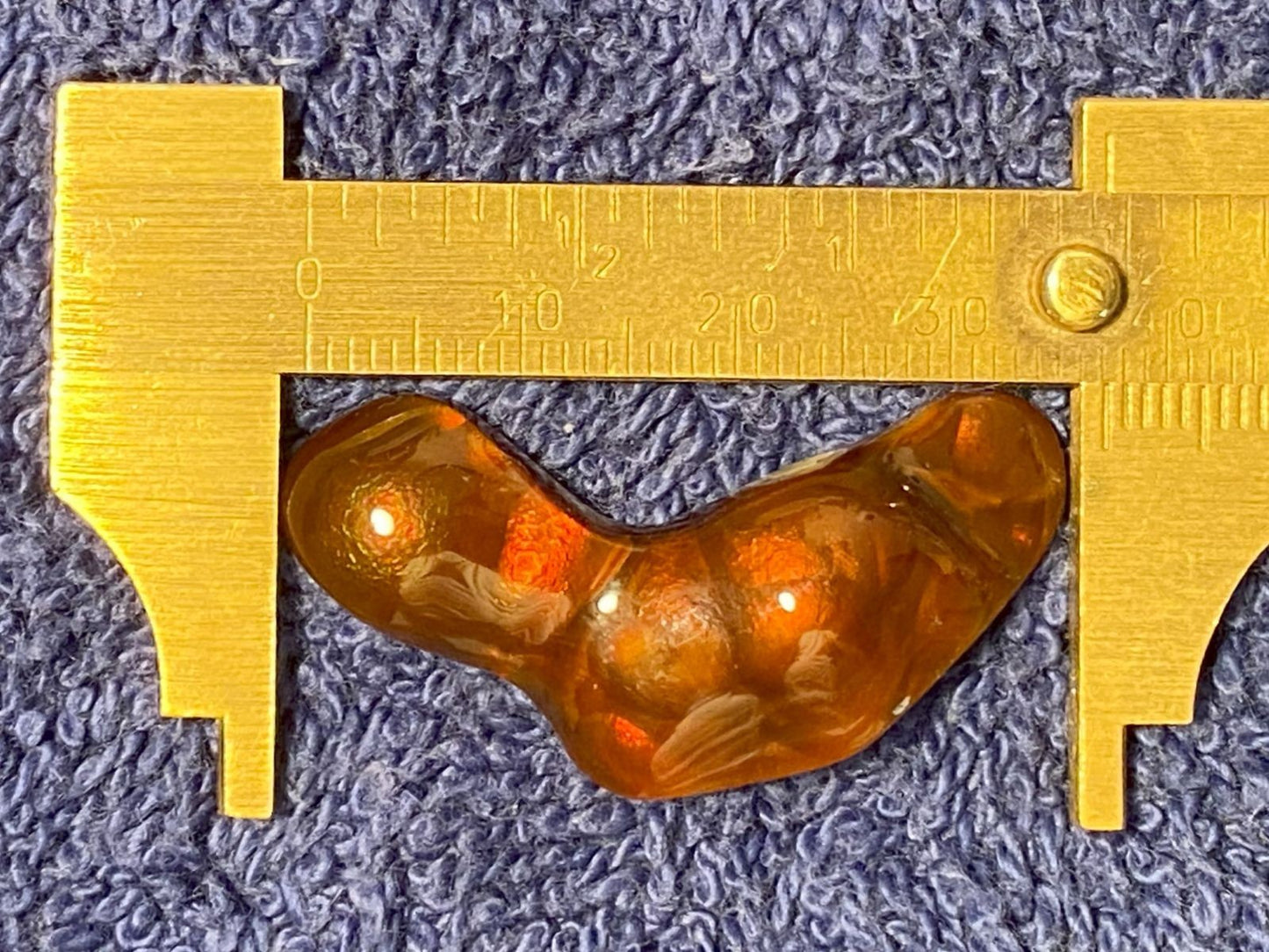 Orange colored fire agate gemstone with held by a brass caliper on a textured blue background