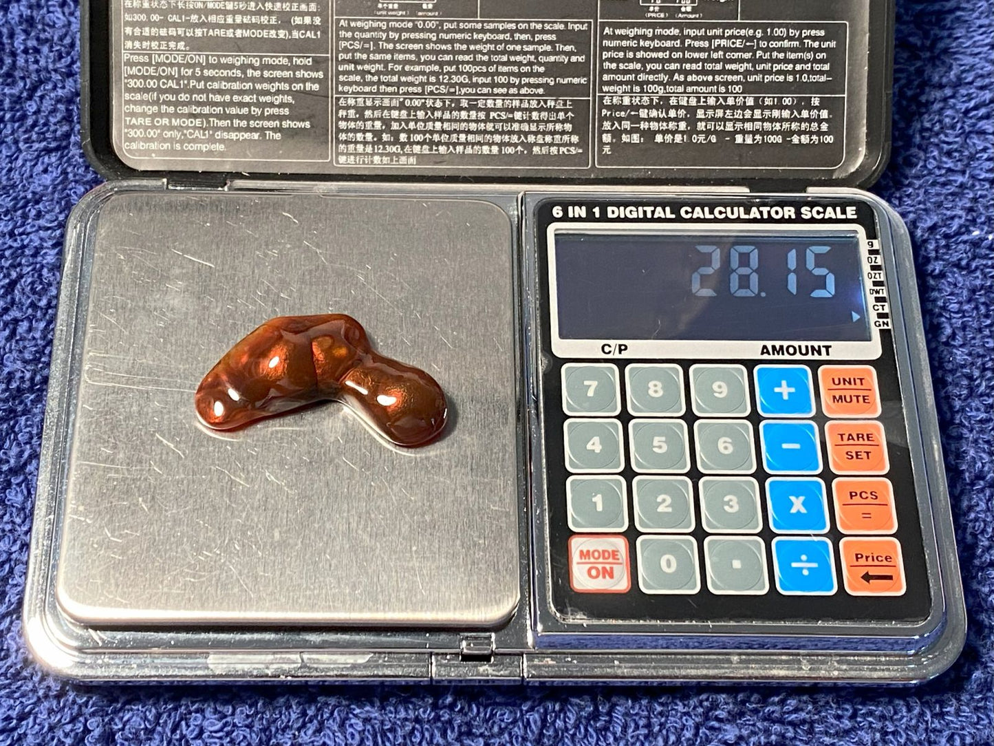 Digital calculator scale with a stone on it, displaying weight '28.15' carats
