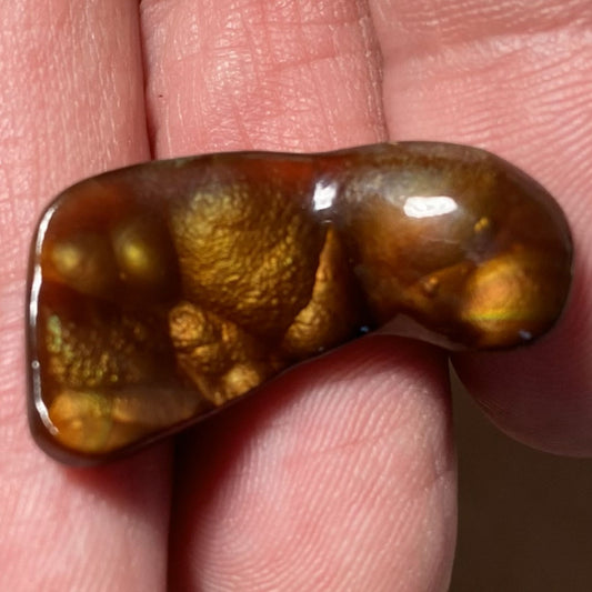 Fire agate gemstone held between fingers against a skin background