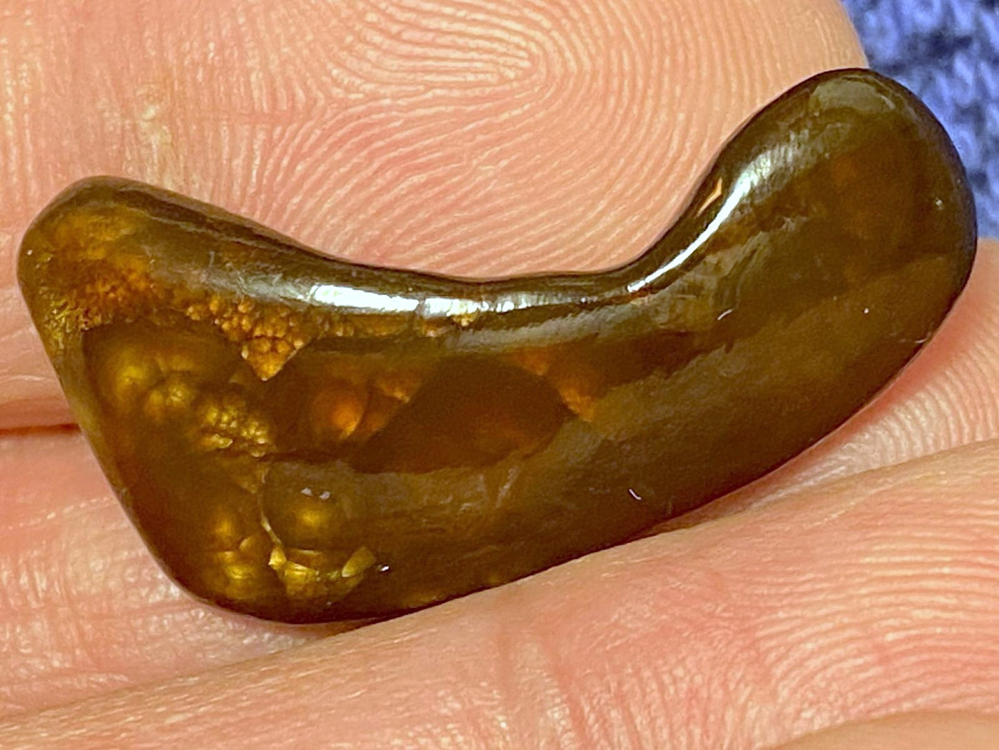 Bottom of Deer Creek Fire Agate Gemstone held between fingers with a blurred background