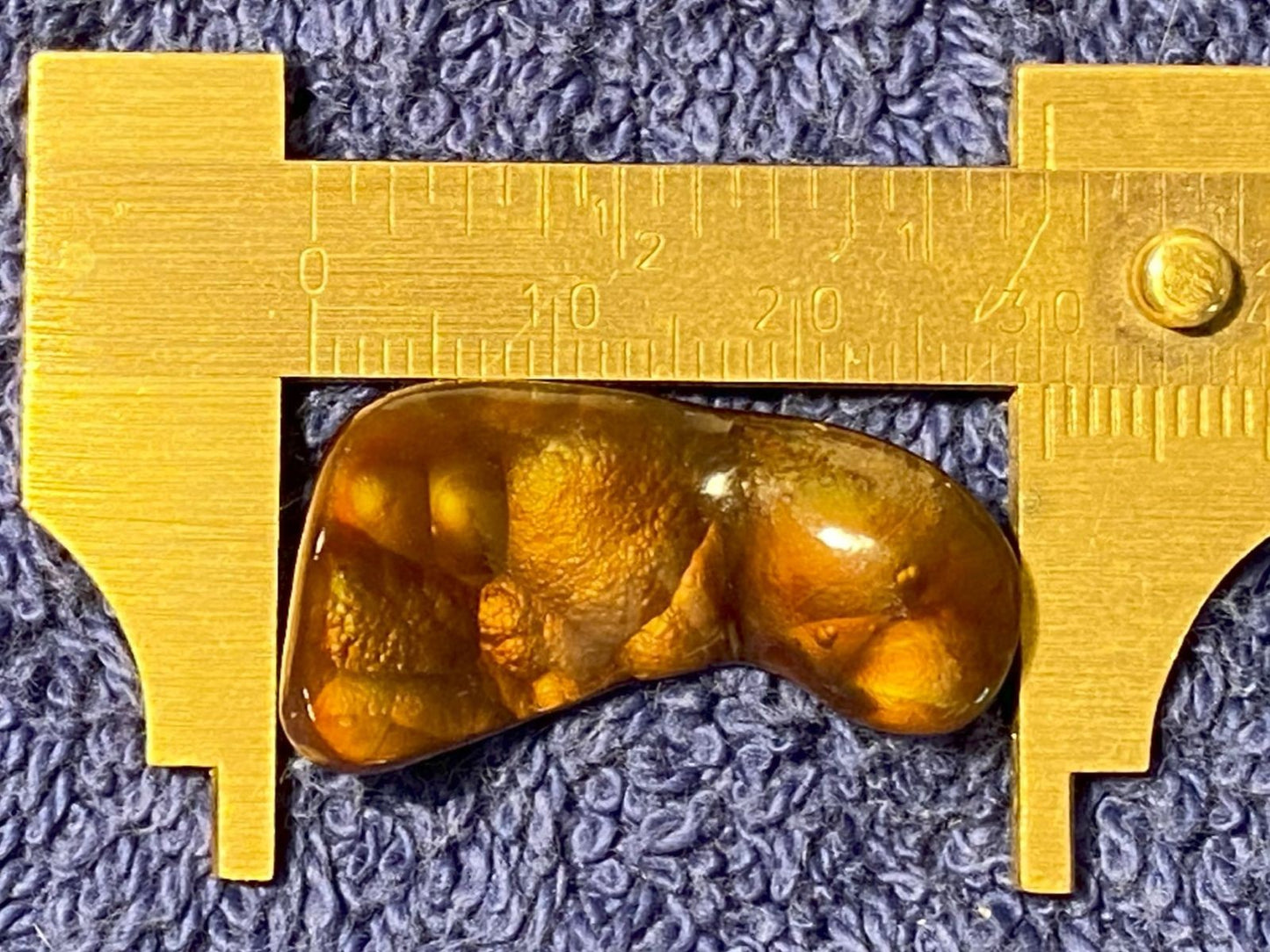 Deer Creek Fire Agate Gemstone between two gold calipers on a textured blue background