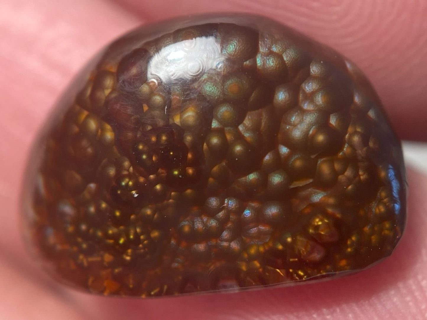 Close-up of a brownish-red Deer Creek Fire Agate Gemstone with a textured surface on a pink background