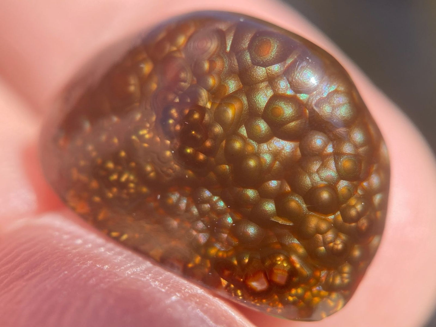 Close-up of a brownish Deer Creek Fire Agate Gemstone held between fingers