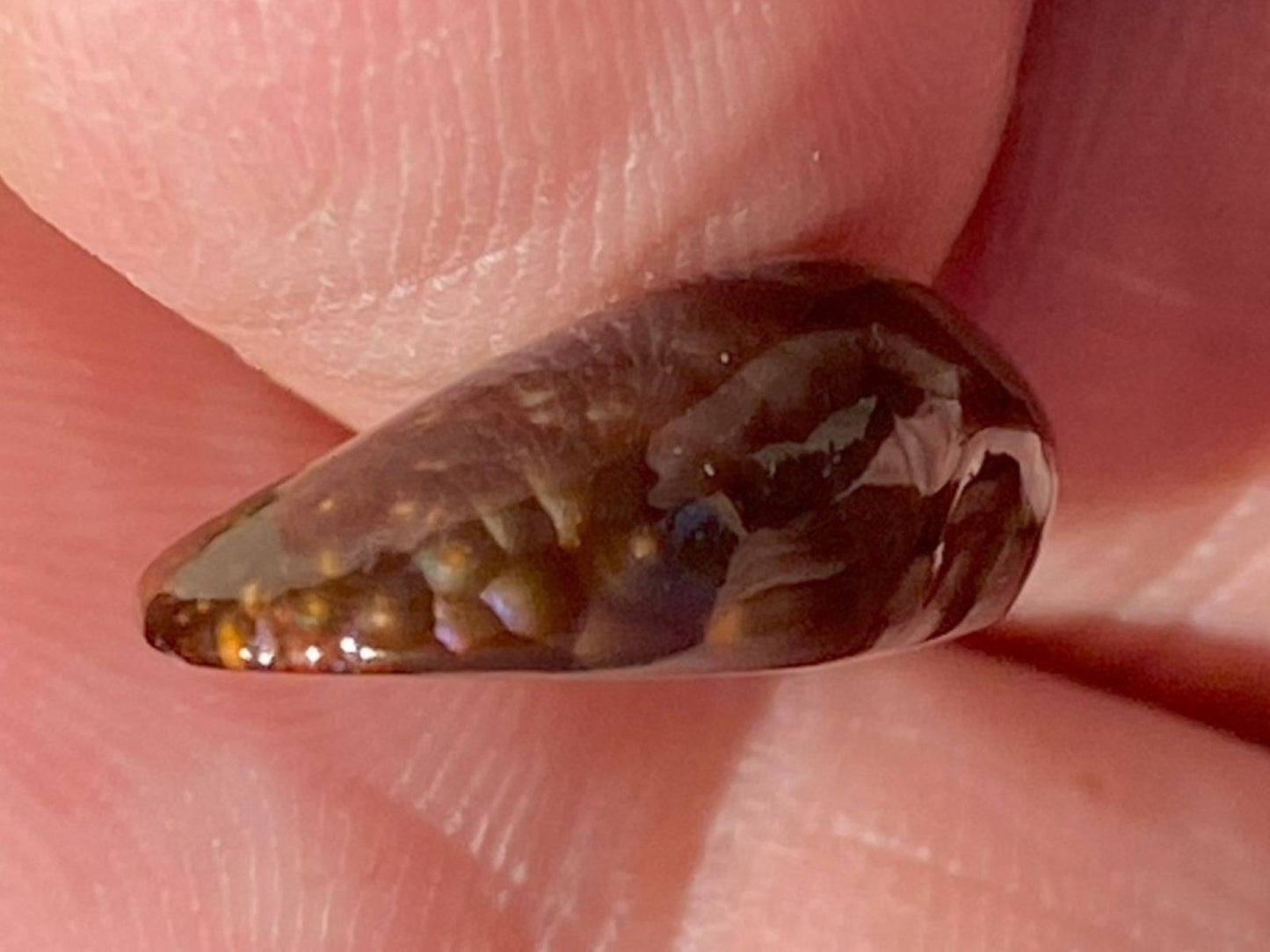 side view of Deer Creek Fire Agate Gemstone held between fingers