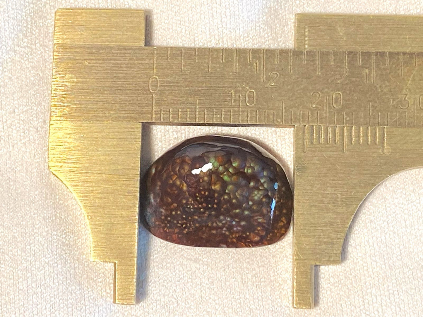 Deer Creek Fire Agate Gemstone being measured with a brass caliper on a white background