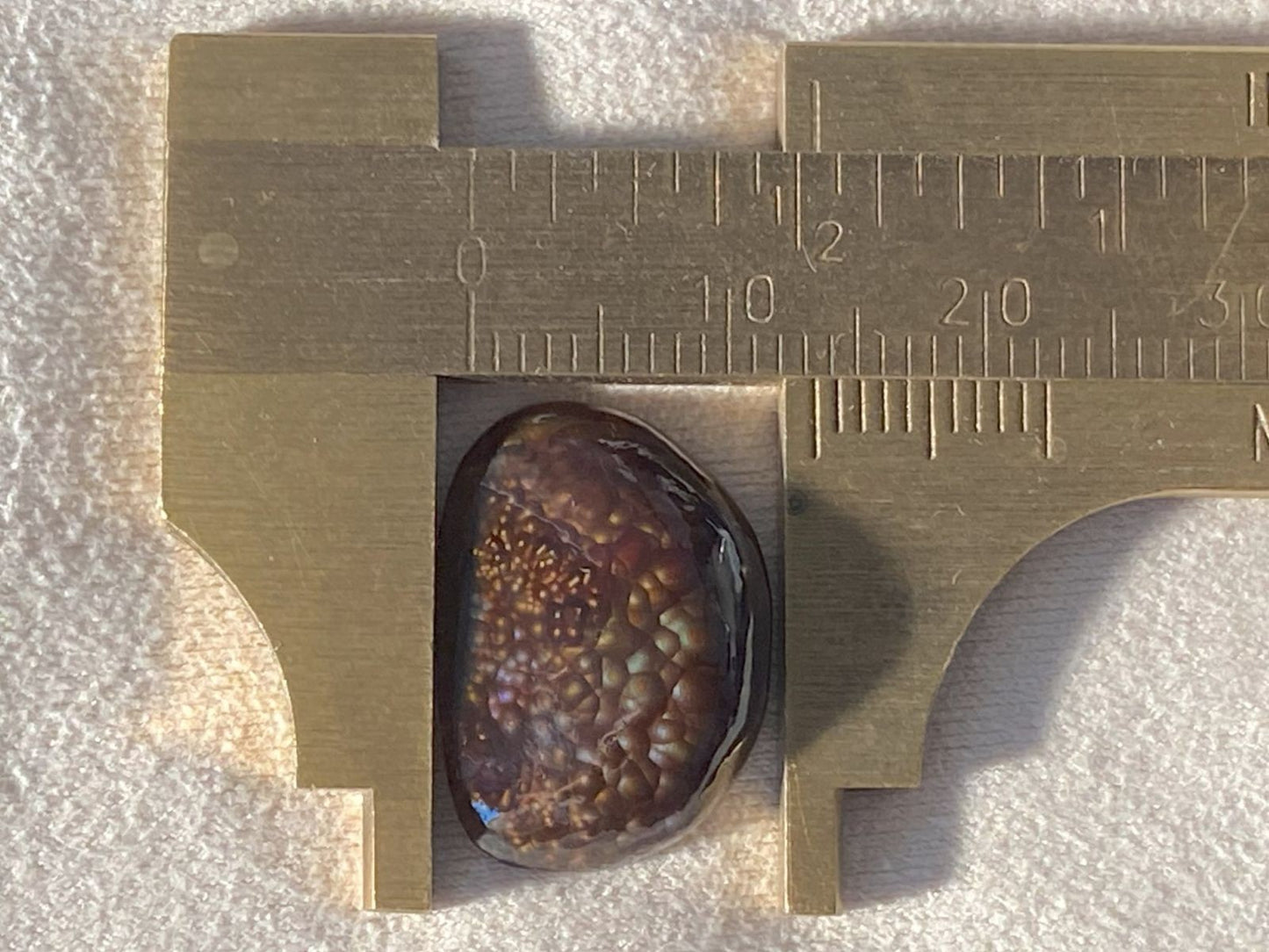 Deer Creek Fire Agate Gemstone with a vernier caliper on a textured surface
