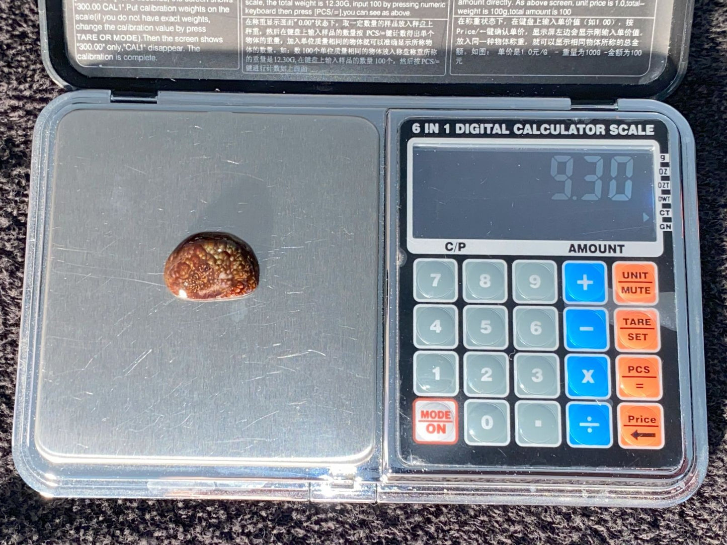 Digital calculator scale with a Deer Creek Fire Agate Gemstone on it