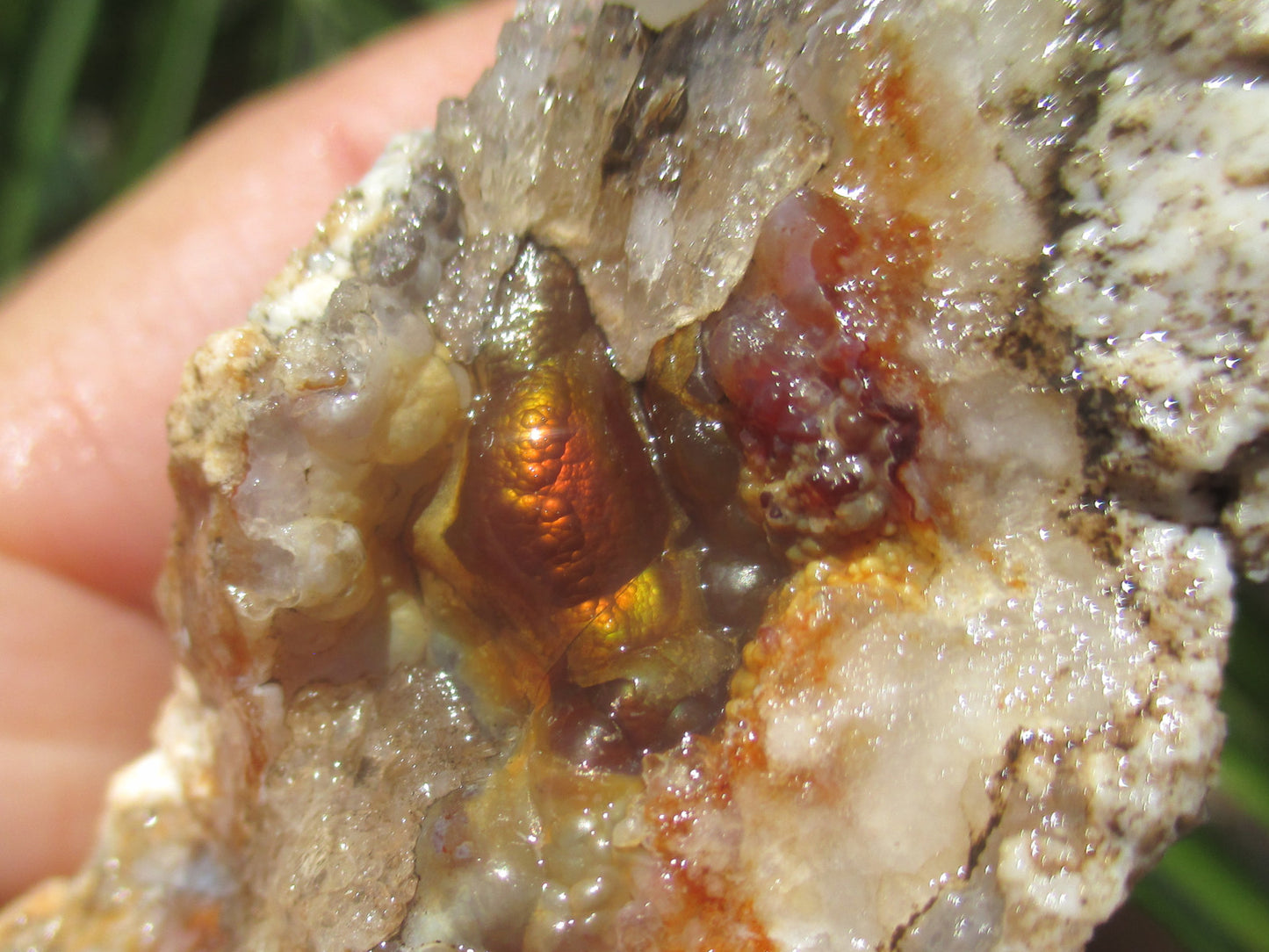 Close-up of a hand holding a crystal with red and brown fire agate inclusions.