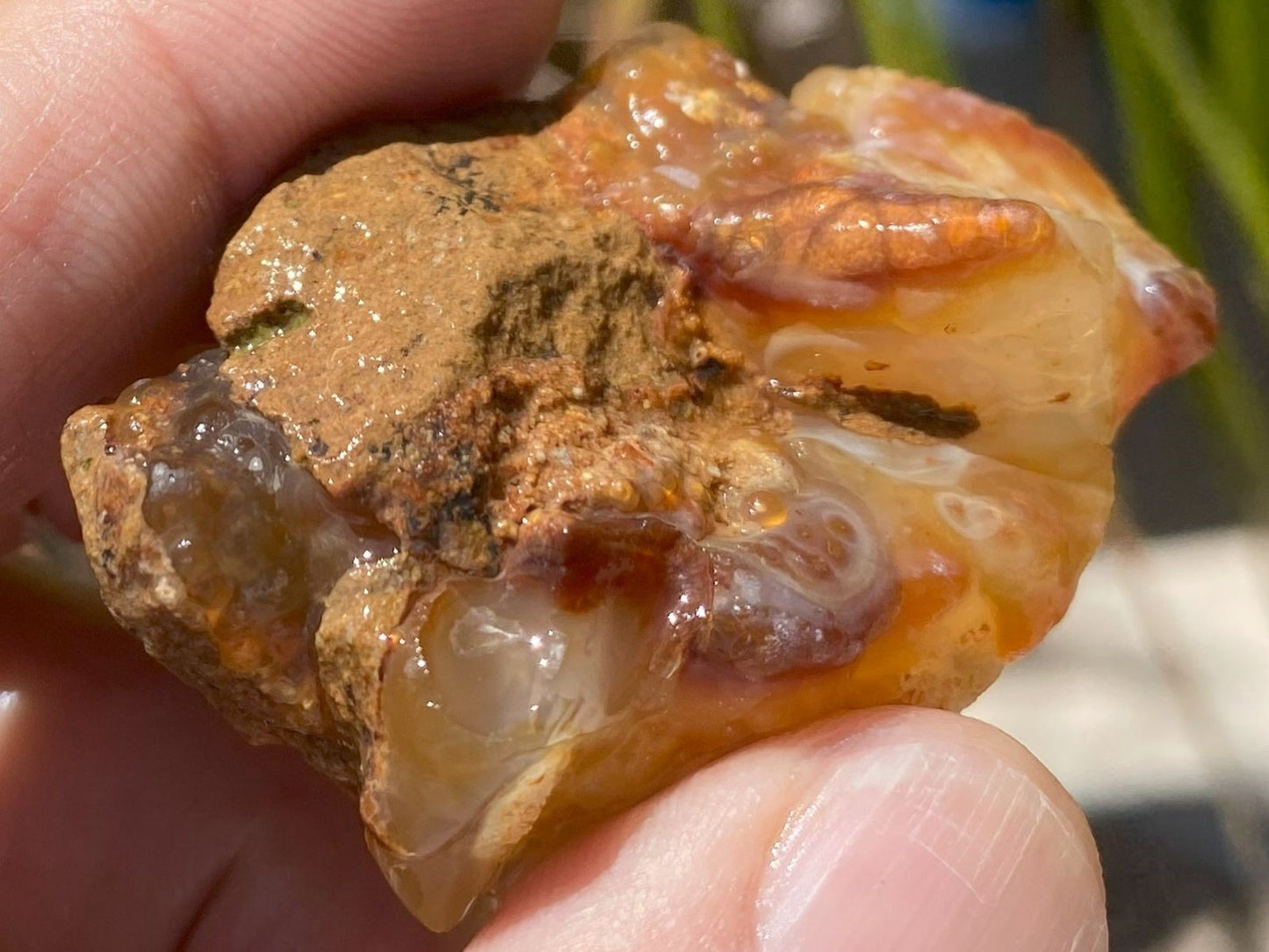 Close-up of a hand holding a rough, orange-brown crystal rock.