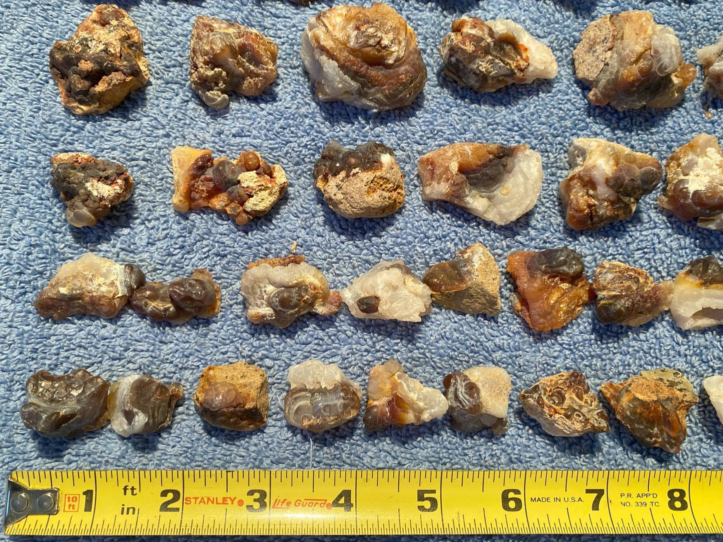 Collection of various sized rocks on a blue textured surface with a measuring tape at the bottom.