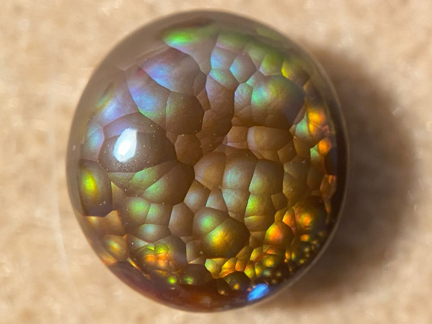 Close-up of a colorful, iridescent Aguascalientes Fire Agate Gemstone on a beige background