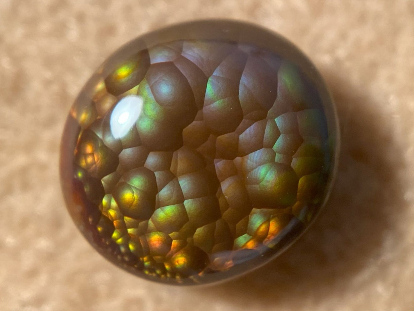 Close-up of a colorful, iridescent Aguascalientes Fire Agate Gemstone on a beige surface
