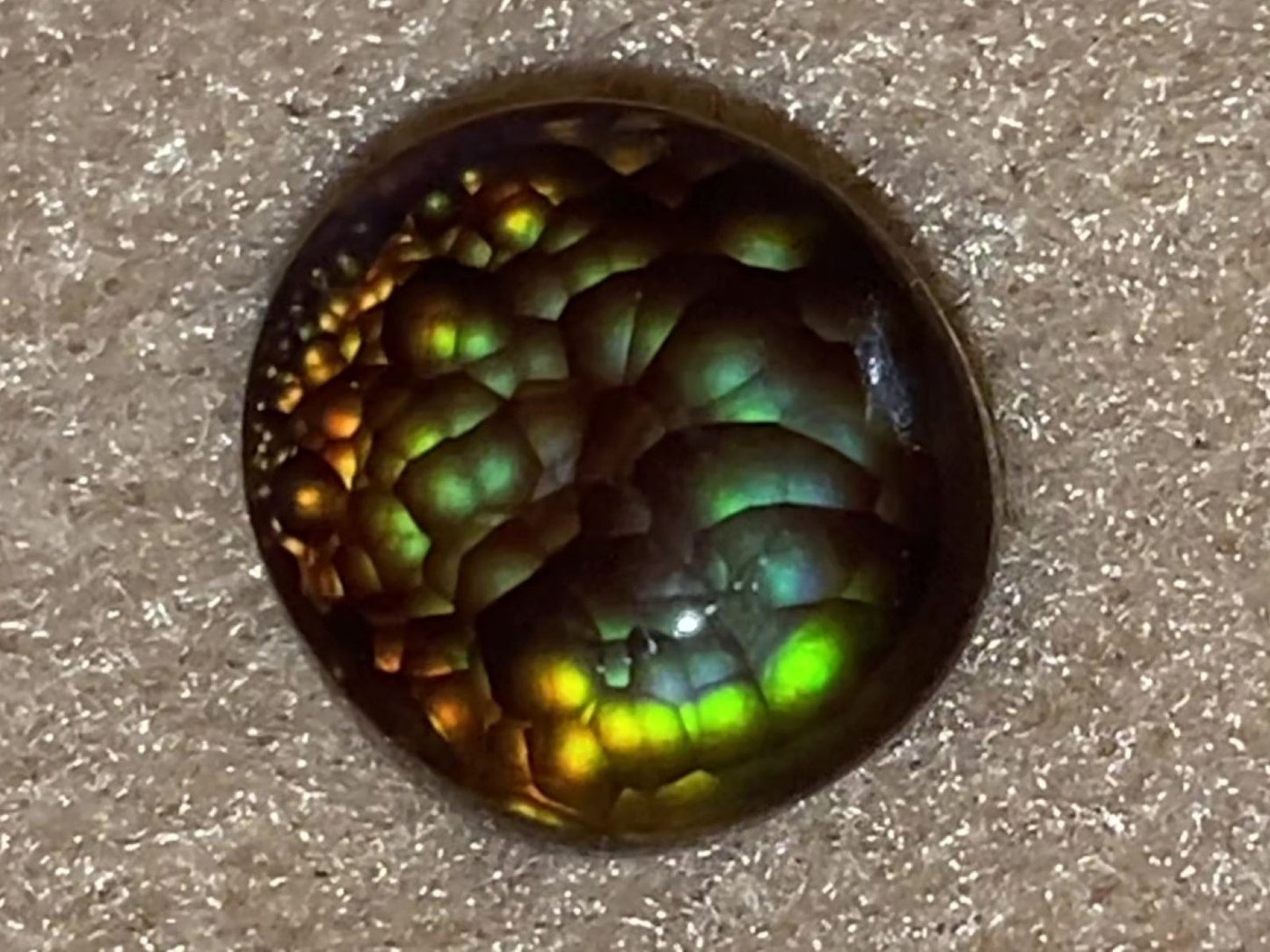 Close-up of a colorful, iridescent Aguascalientes Fire Agate Gemstone on a textured surface