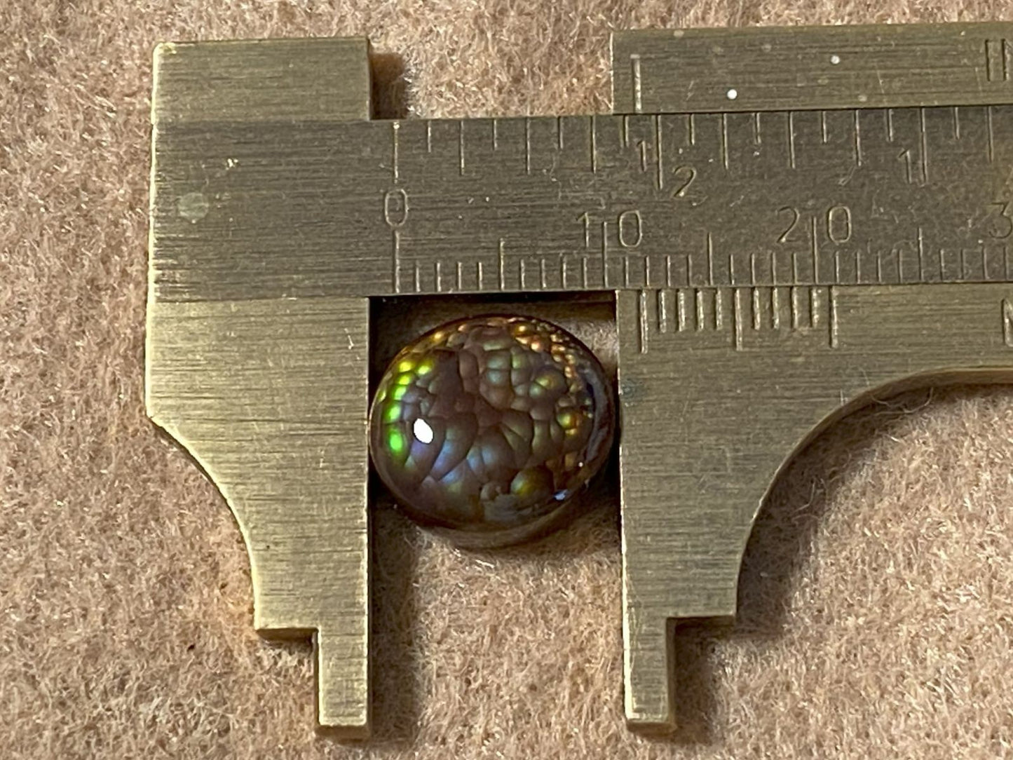 Close-up of a measuring tool with a Aguascalientes Fire Agate Gemstone inside, on a textured surface.