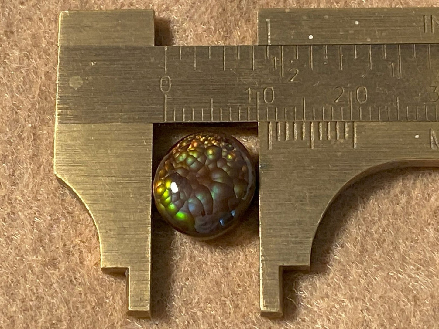 Close-up of a measuring tool with a colorful Aguascalientes Fire Agate Gemstone inside, on a brown background