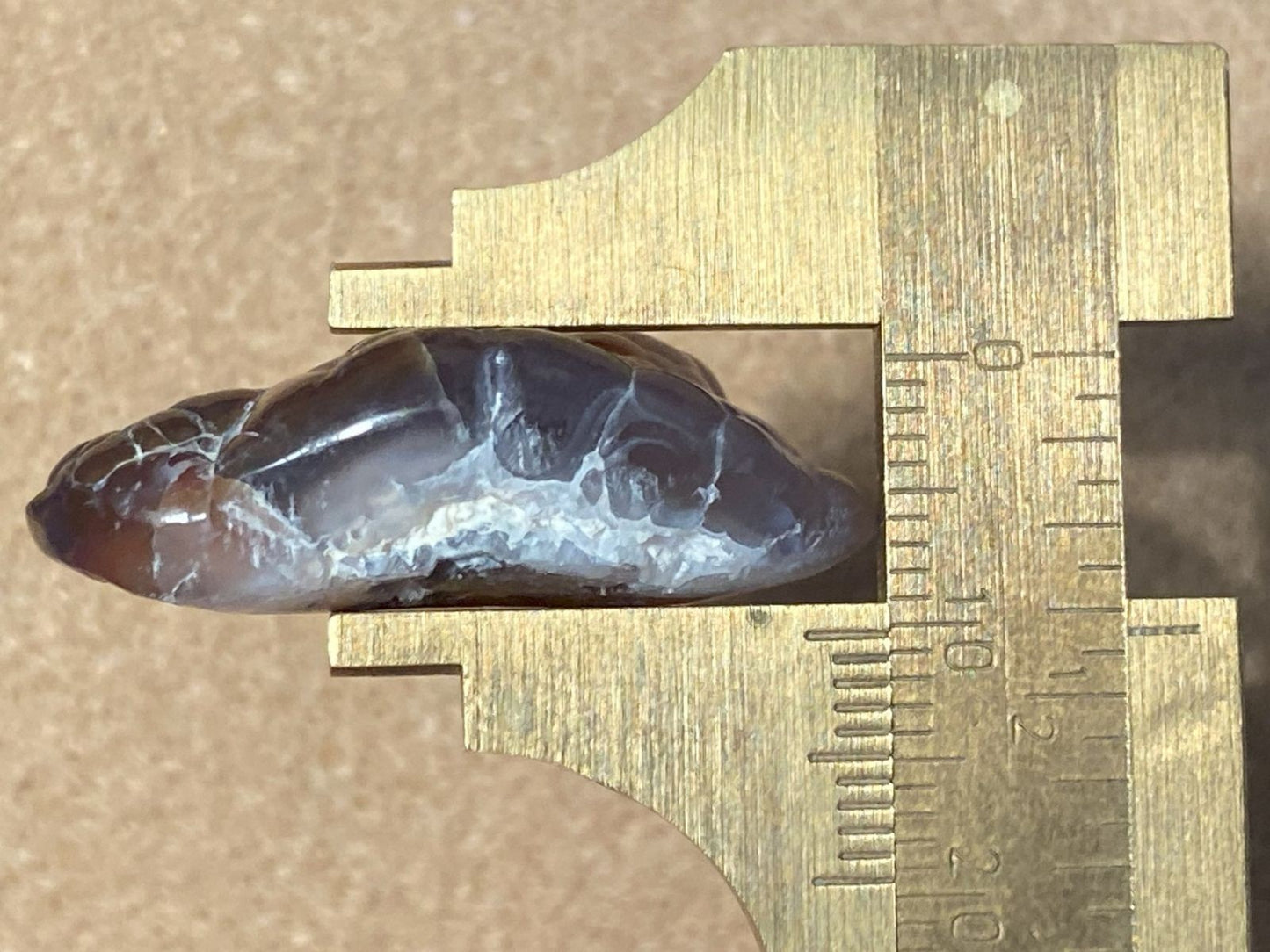 Mineral sample on a brass vernier caliper against a brown background
