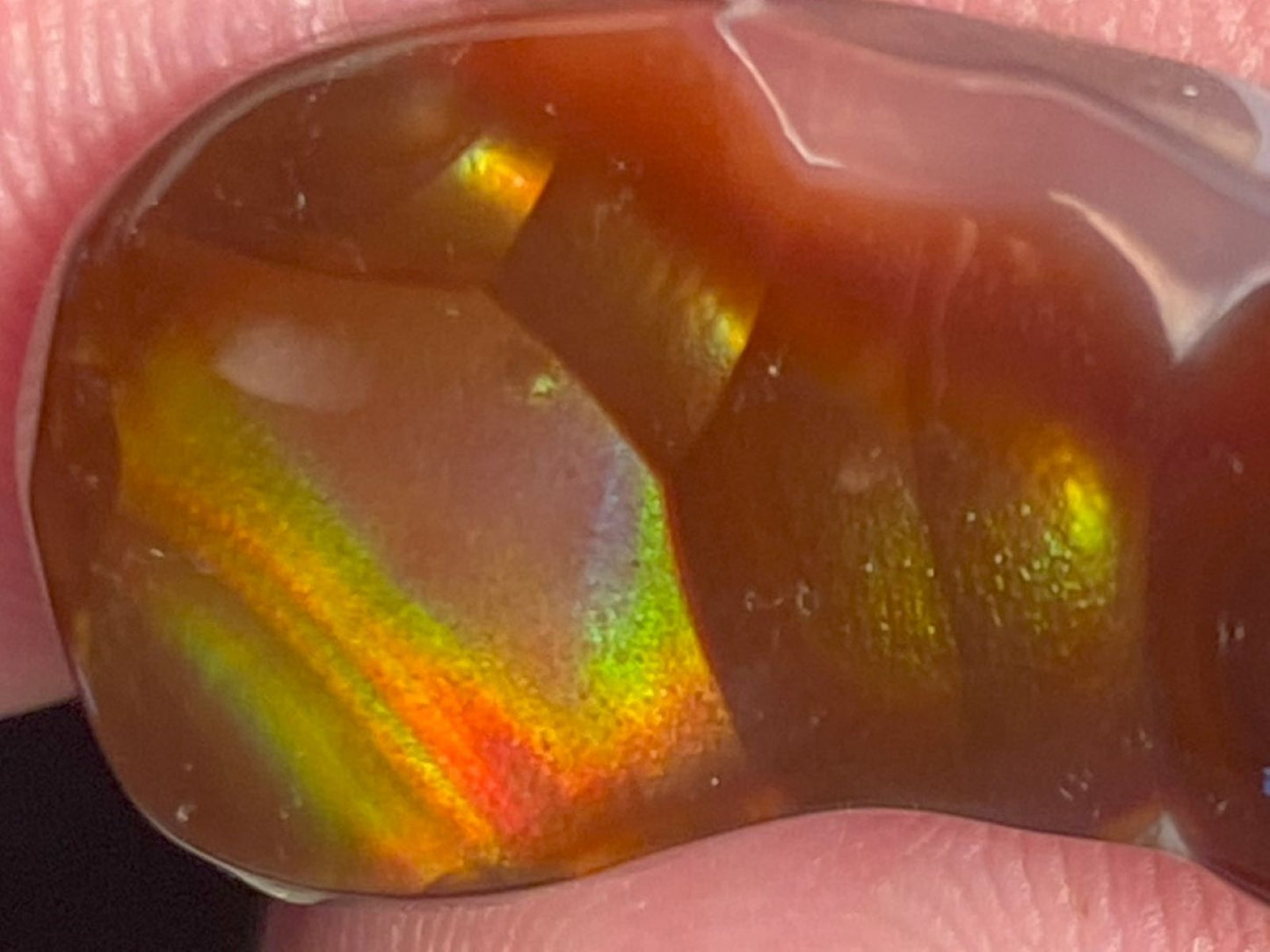 Multicolored Aguascalientes fire agate gemstone held between fingers with a blurred background