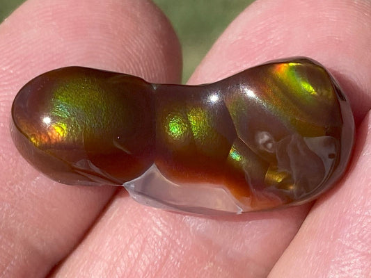 Multicolored Aguascalientes fire agate gemstone held between fingers with a blurred background