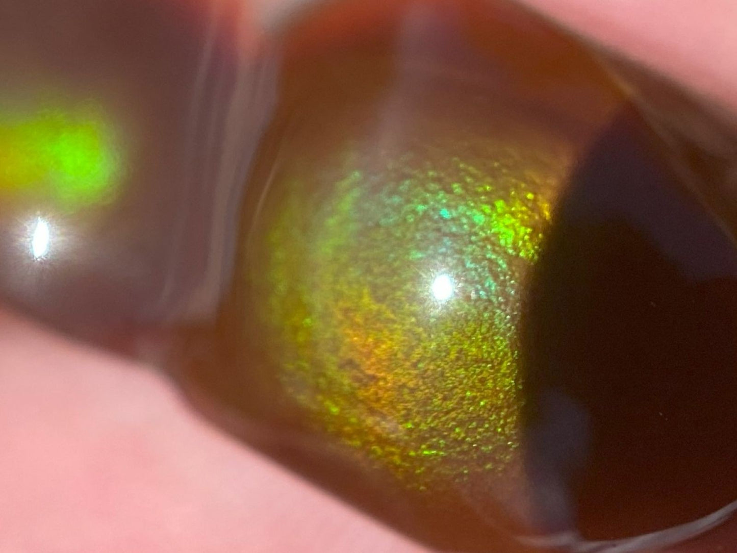 Close-up of a reflective, multicolored Aguascalientes fire agate gemstone held between fingers