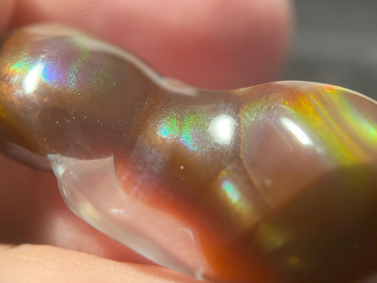 Close-up of a rainbow-colored Aguascalientes fire agate gemstone held between fingers