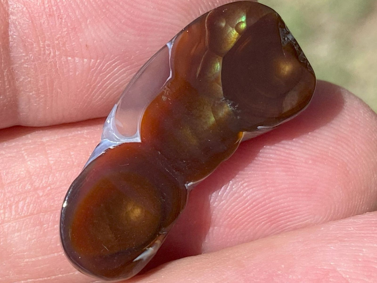 Close-up of the bottom of a Aguascalientes fire agate gemstone held between fingers with a blurred natural background