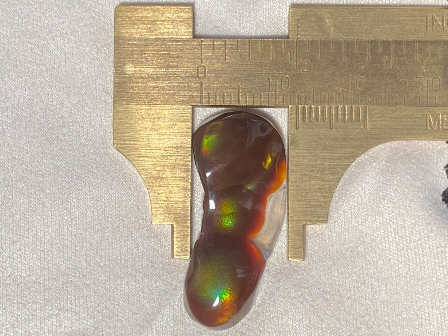 Aguascalientes fire agate gemstone being measured with a brass caliper on a light gray background