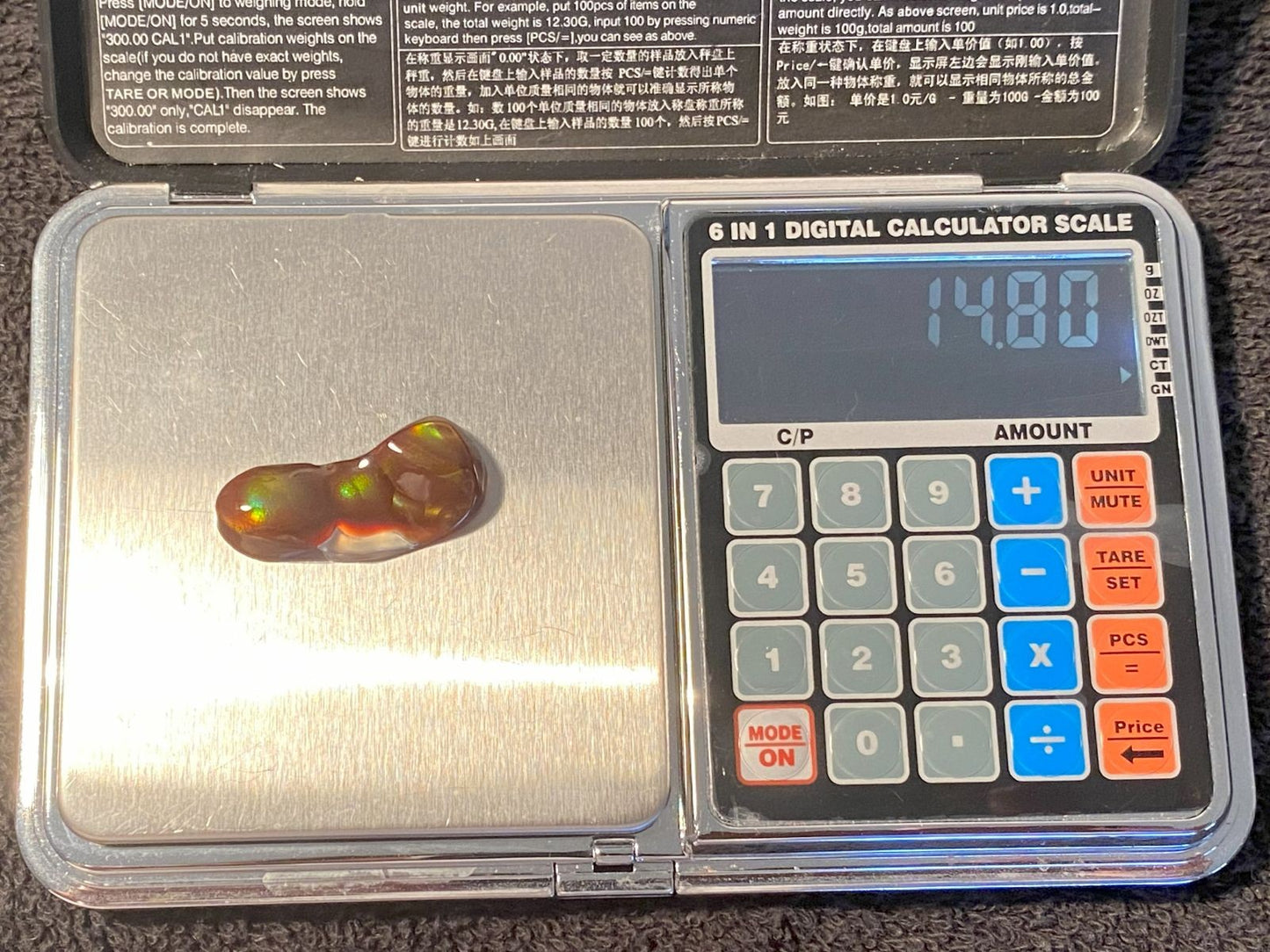 Aguascalientes fire agate gemstone on a digital calculator scale with visible readings of 14.80 carats