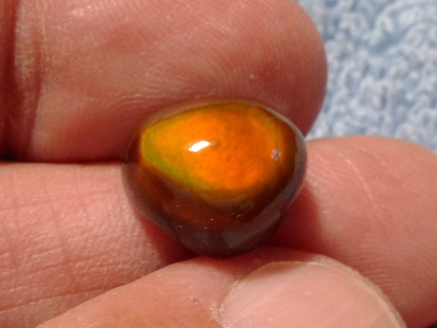 Close-up of a hand holding a multicolored stone with an orange and brown hue.