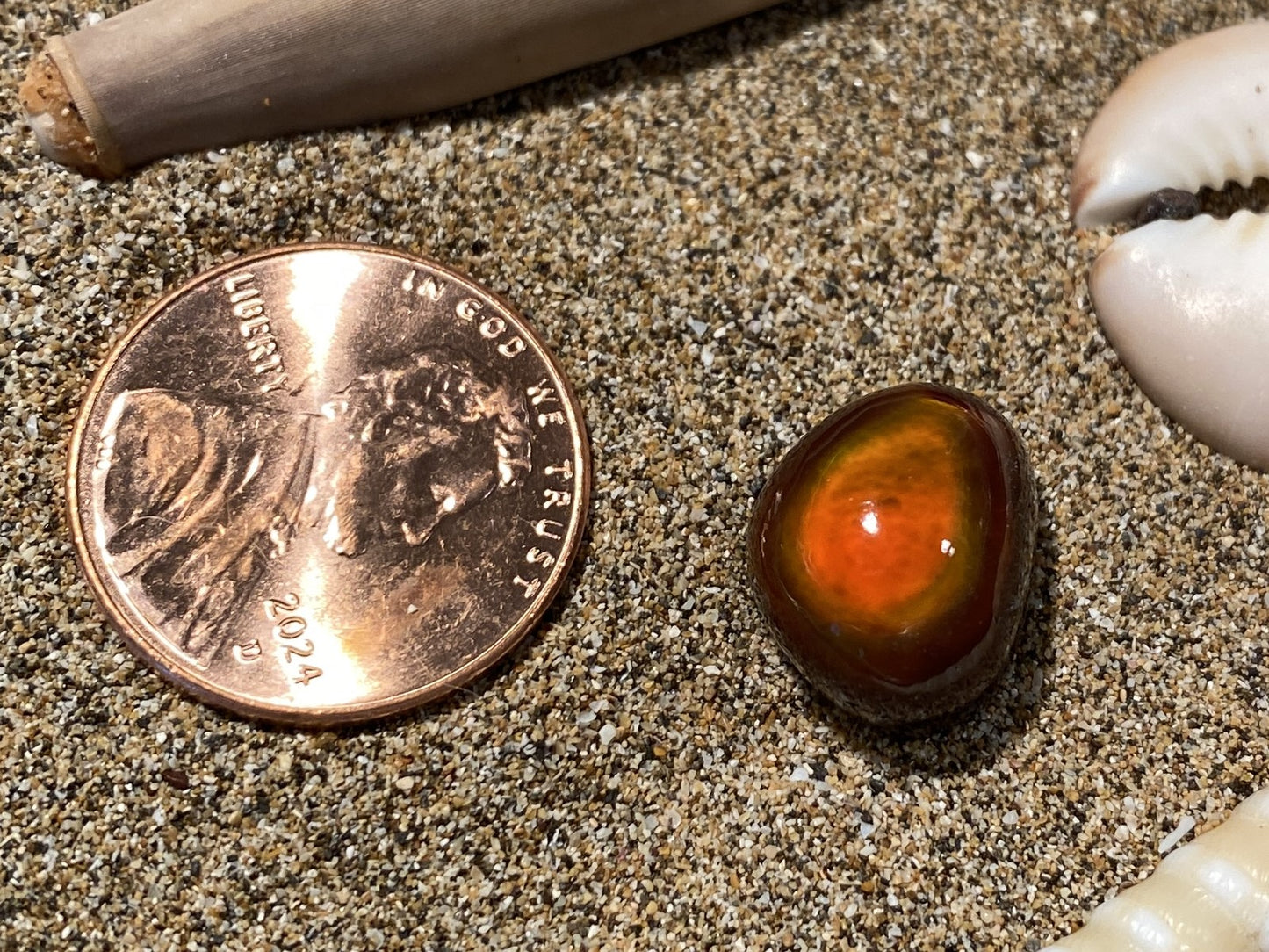 Penny next to a small amber-colored Slaughter Mountain Fire Agate Gemstone on sandy surface