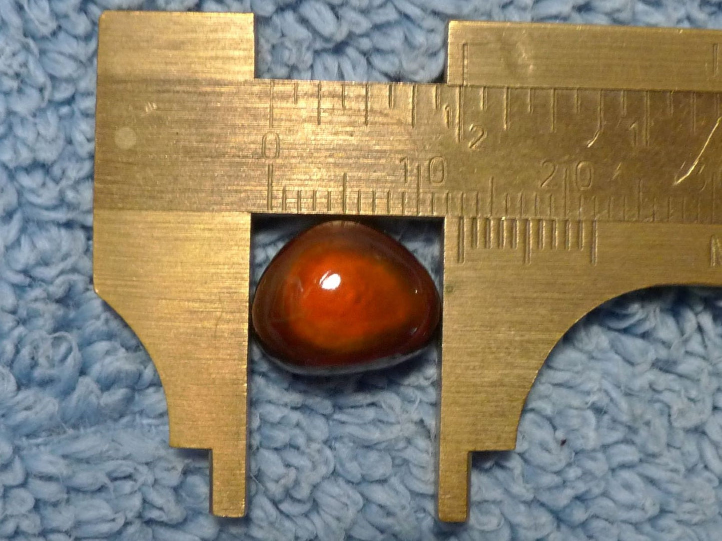 Gold-colored caliper measuring a red-orange gemstone on a blue textured background