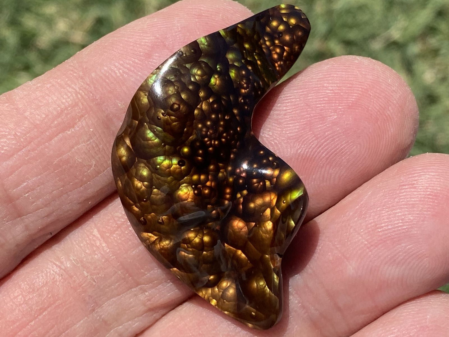 Polished fire agate gemstone held in a hand with a blurred natural background
