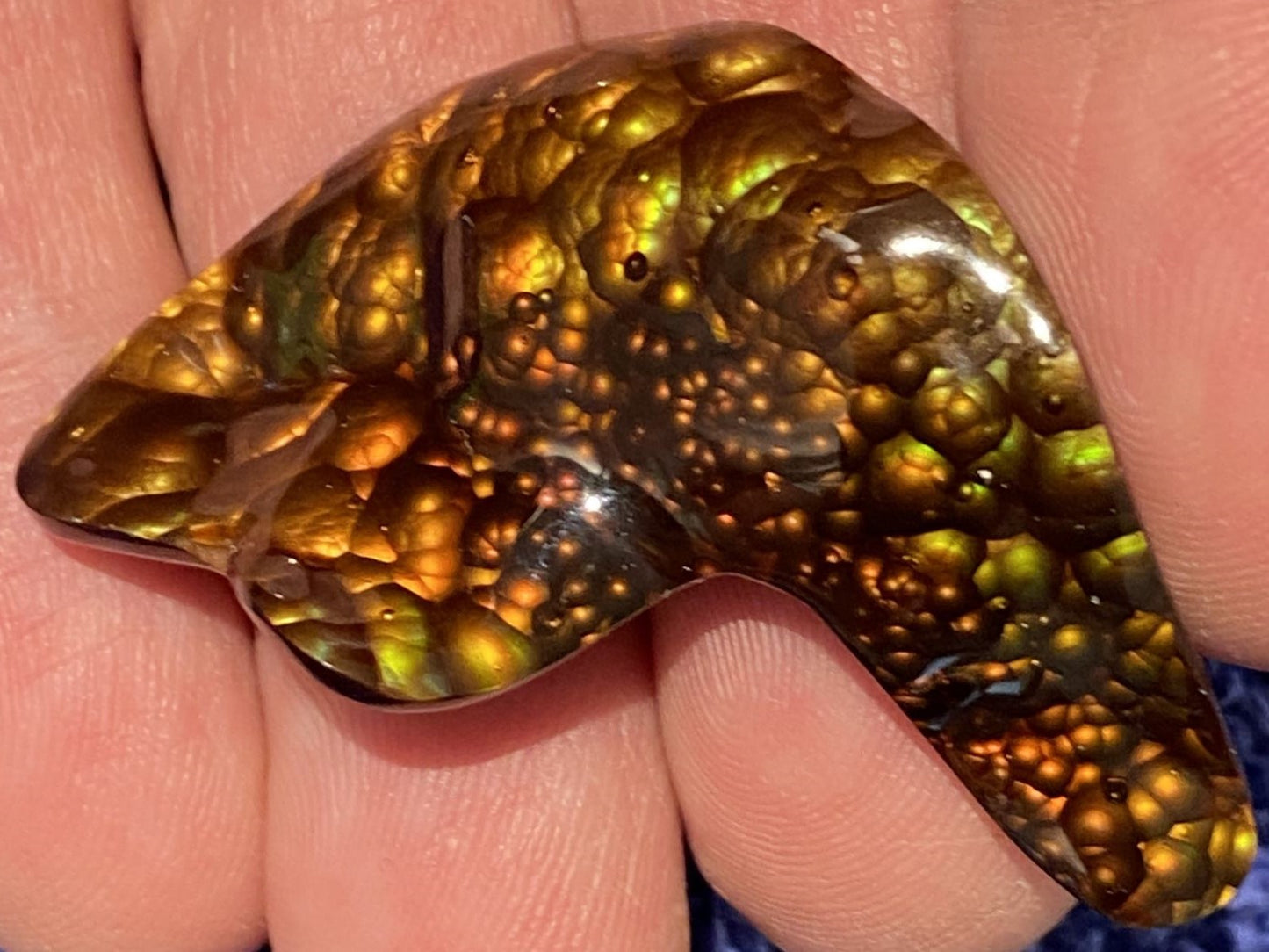 Polished multicolored fire agate gemstone held between human fingers