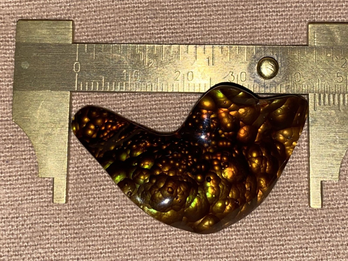 Orange and green colored fire agate gemstone shaped like a bird with a ruler for scale on a brown background