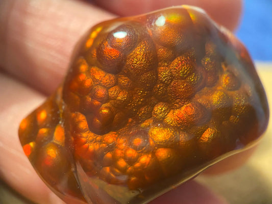 Close-up of a polished Slaughter Mountain fire agate gemstone held in a hand with a blurred background