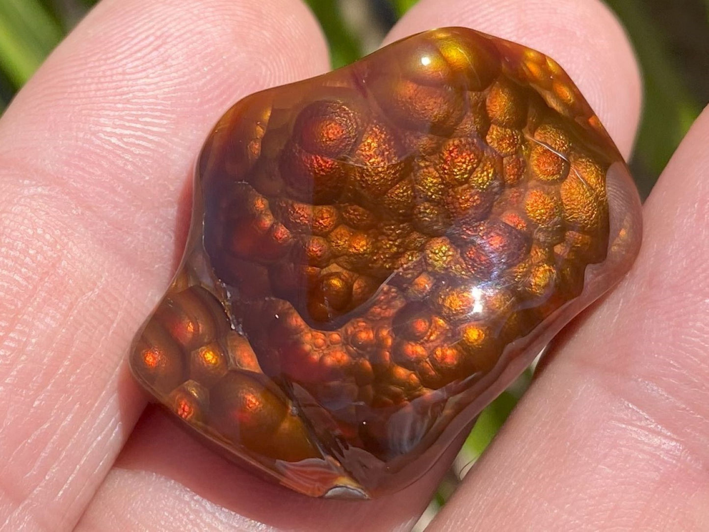 Close-up of a hand holding a polished firey red Slaughter Mountain fore agate gemstone with an intricate bubble pattern.