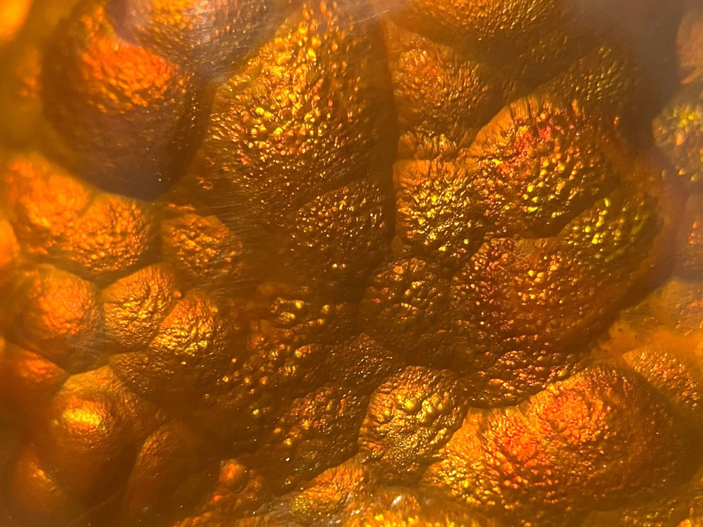 Close-up of a textured orange, gold and green fire pattern within a Slaughter Mountain fire agate gemstone surface with a metallic sheen.